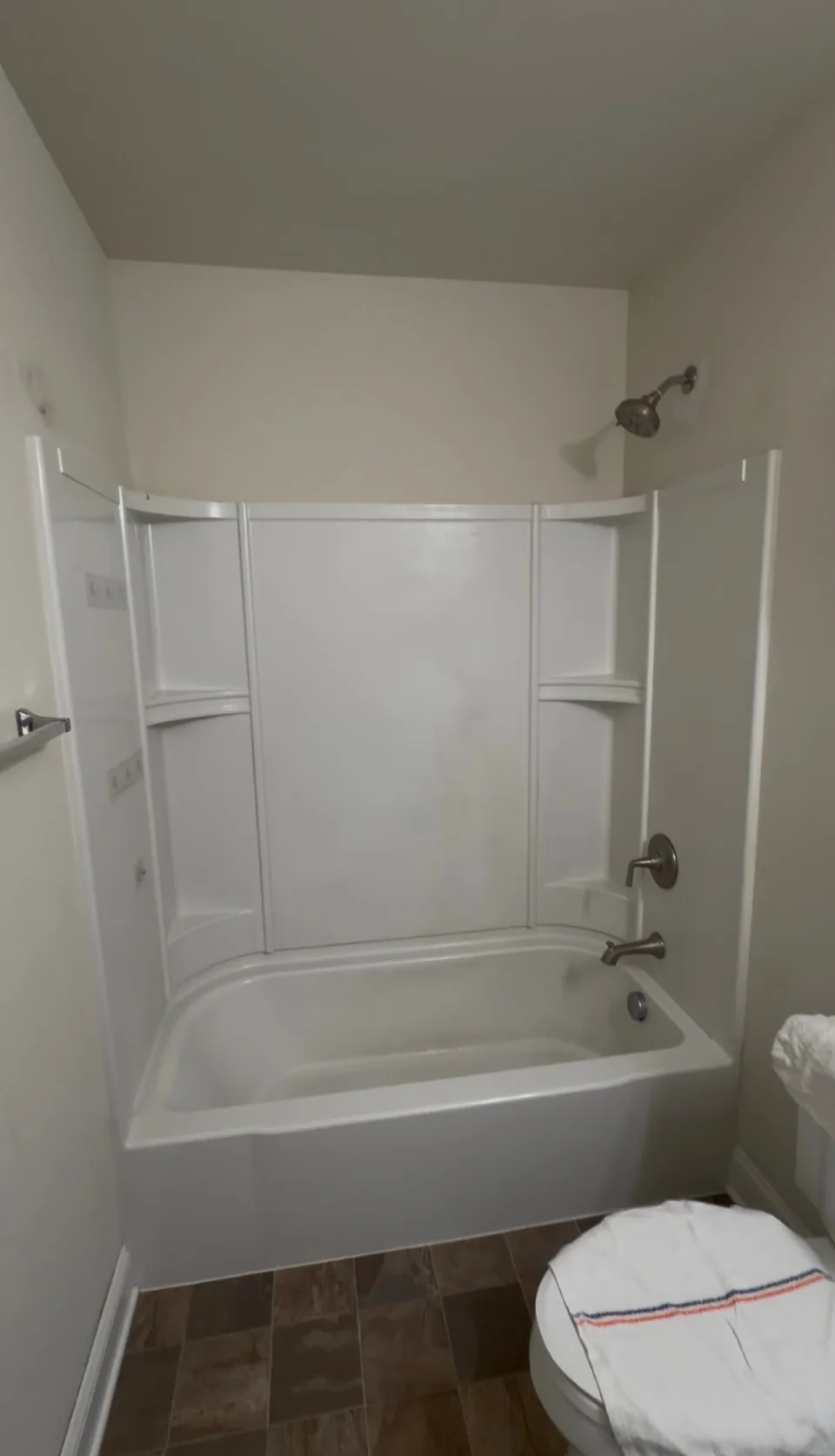 Before: bathroom with a white bathtub and molded shower surround, painted walls, and brown floor tile.