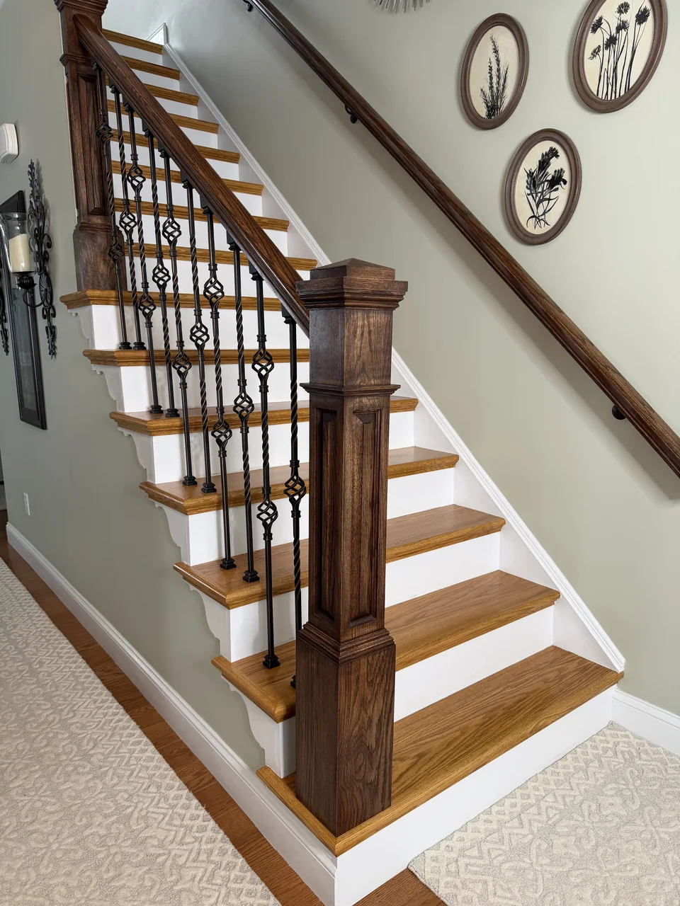 Staircase with wood treads, white risers, dark wood posts and handrails, and black decorative balusters.