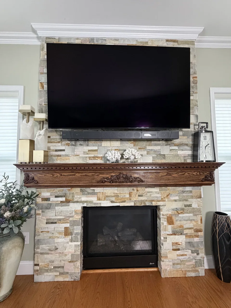 Fireplace with a staggered stone-faced surround, a dark carved wooden mantle, and white trim along the top.