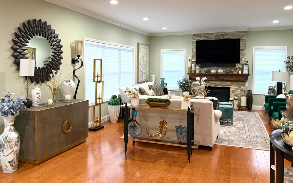Living room with warm wood flooring, light walls, white ceiling trim, and a stone-faced fireplace behind the seating area.