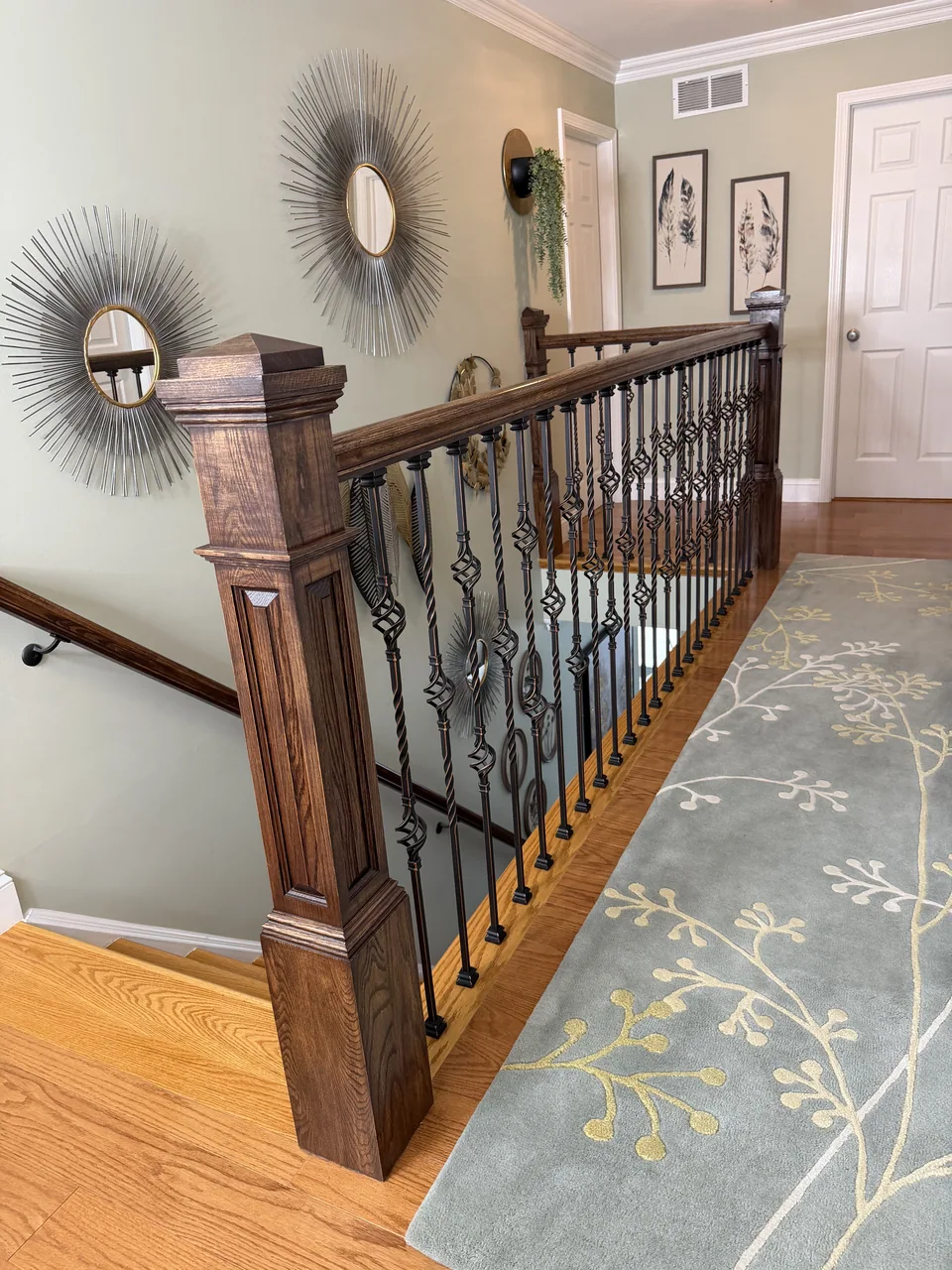 Finished upstairs landing with wood flooring, dark wood posts and rail, and black decorative balusters overlooking the stairs.