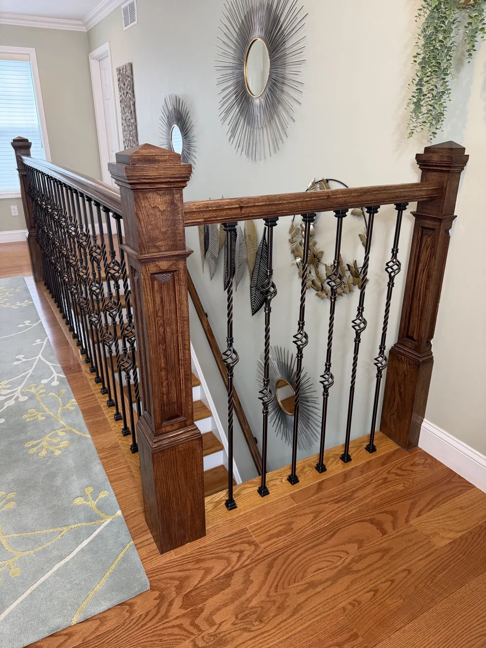 Wood flooring at an upstairs landing, bordered by dark wood posts and rails with black decorative balusters.