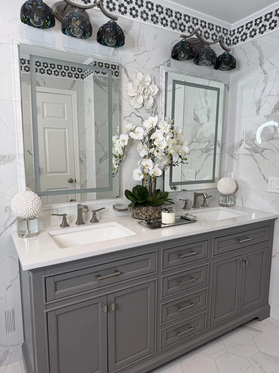 Veined wall tile and a black and white mosaic border above a double vanity.