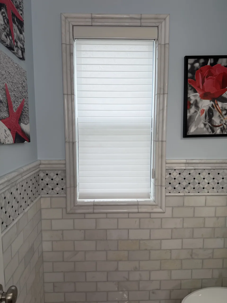 Light marble trim framing a bathroom window above rectangular wall tile and a black and white patterned border.